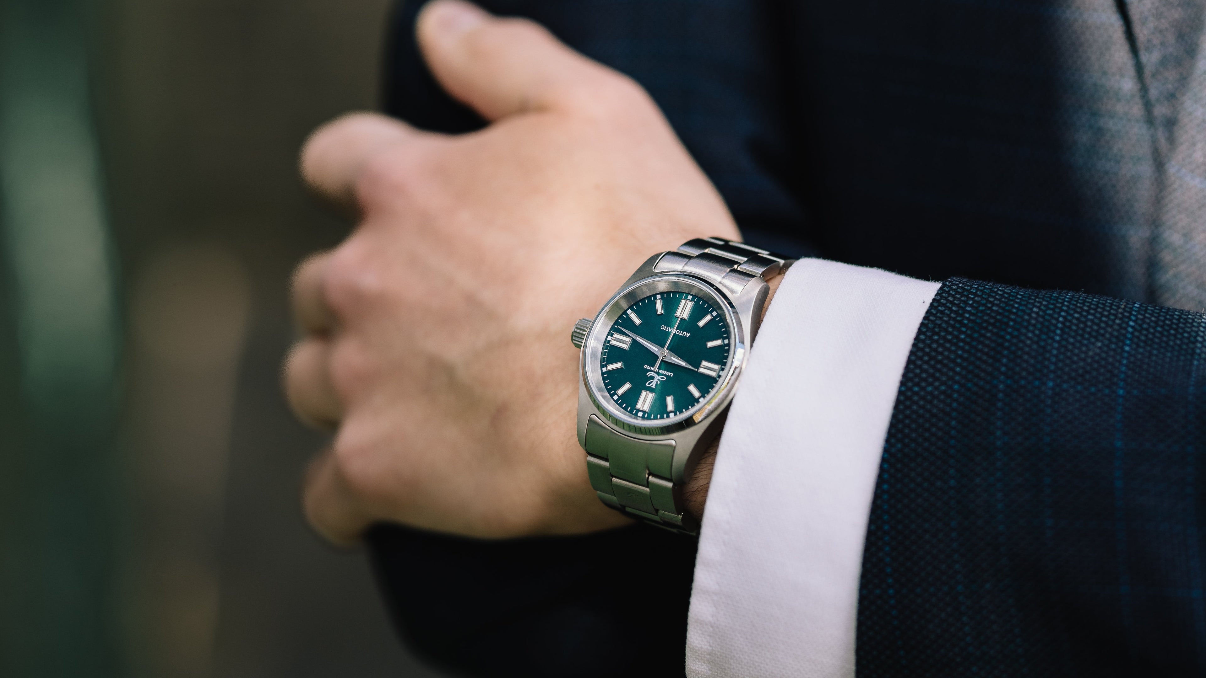 Close-up of a person wearing a dark suit with a green watch on a blurred background